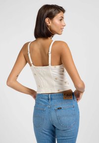 Hvit blomstret smocket croptopp med justerbare stropper, kombinert med høyt midje blå denim jeans med lærpatch bak og klassiske lommer.
