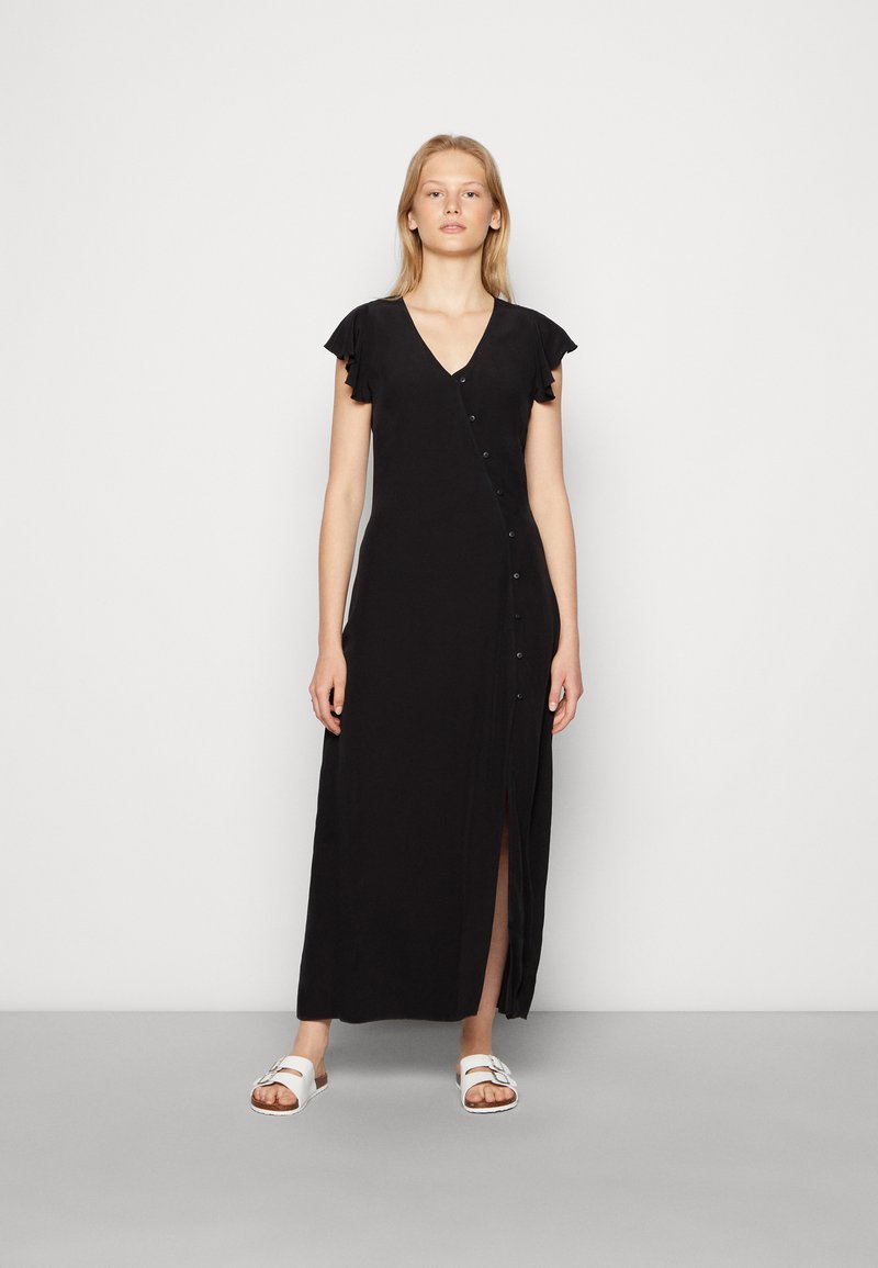 Vestido preto, até ao joelho, com decote em V, mangas leves e botões na frente. O tecido parece suave e cai levemente.