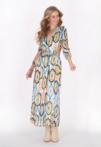 Rochie maxi cu un model geometric colorat, decolteu în V, mâneci lungi, talie decupată, realizată dintr-un material ușor, asortată cu botine bej.