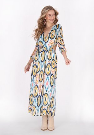 Maxikleid mit einem bunten geometrischen Muster, V-Ausschnitt, langen Ärmeln, ausgeschnittenem Taillenbereich, aus leichtem Stoff, kombiniert mit beigen Ankle Boots.