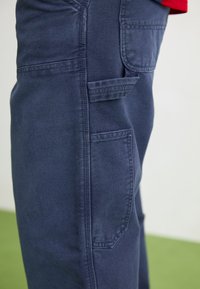 Pantalones de carga azul marino hechos de mezclilla con una textura suave. Presentan grandes bolsillos laterales y costuras reforzadas para mayor durabilidad.