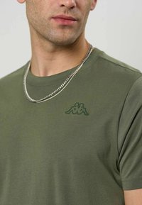 Olivengrønn kortermet t-skjorte laget av mykt stoff, med en grønn brodert logo på venstre bryst og rund hals.