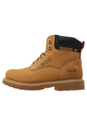 Botas impermeables de color marrón con un cuello acolchado negro, ojales metálicos y detalles de costura. Suela de goma con un patrón de dibujo distintivo.
