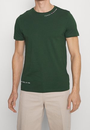 Grünes Baumwoll-T-Shirt mit kurzen Ärmeln, Rundhalsausschnitt, mit weiß gesticktem Logo am Kragen und Text am Saum. Glatte Textur.