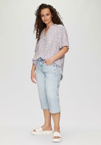Jasnofioletowa koszula w kwiatowy wzór z krótkim rękawem, zestawiona z jasnoniebieskimi jeansami o skrócone nogawki i białymi klapkami, tworzy swobodny look.