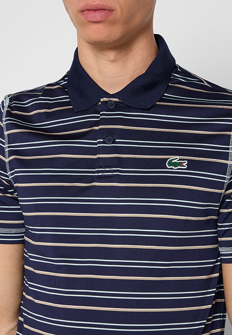 Polo rayé bleu marine avec un col boutonné, des lignes horizontales en bleu clair et beige, et un petit logo de crocodile vert sur la poitrine.