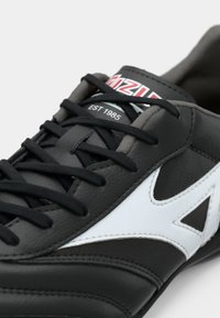 Črne usnjene teniske z belimi detajli, z črnimi vezalkami in mehko teksturo. Logotip na jezikcu prikazuje "EST 1985" v rdeči barvi.