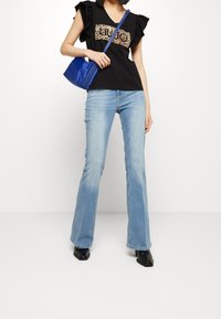 Zwart top met gerimpelde mouwen en een panterprintpaneel, lichtblauwe flare jeans en een kleine blauwe handtas. Zwarte vierkante schoenen maken de look compleet.