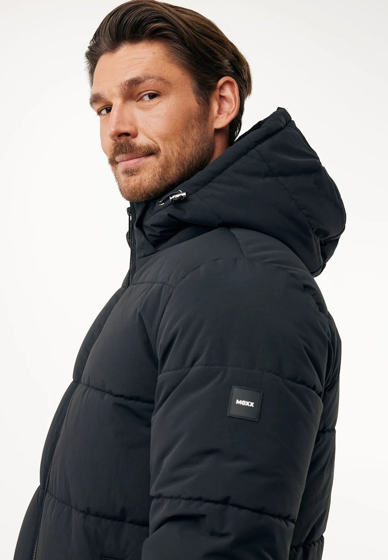 Schwarze, puffy Jacke mit Kapuze, gestepptem Design, verstellbarem Kordelzug und Logo-Patch am linken Ärmel. Glatte Textur, warmer Eindruck.