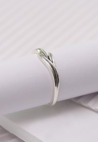 Silberner Ring mit einer glatten, polierten Oberfläche. Er hat ein gedrehtes Design, das zarte Blätter oder Ranken ähnelt, und liegt auf einer weißen Fläche.