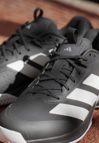 Czarne buty sportowe z fakturowaną cholewką, z trzema białymi paskami, wzmocnionym noskiem, sznurowanym zapięciem i gumową podeszwą.