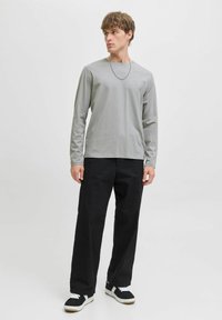 Grijze T-shirt met lange mouwen en een ronde hals, gecombineerd met ruime zwarte broek en zwarte sneakers met witte accenten.