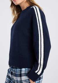 Navy blue sweater made of soft knit fabric with a round neckline, featuring white stripes down the sleeves and a ribbed hem.