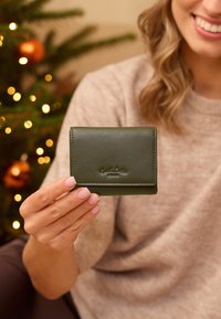 Vihreä nahkainen lompakko, jossa on sileä pinta, taitettavan muotoilun ja kohotetun logon. Pitää suorakaiteen muotoa ja siinä on siisti ommel.