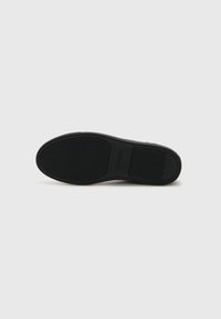 Semelle de chaussure en caoutchouc noir avec un motif de grip texturé, présentant une forme arrondie et un logo de marque. Surface lisse avec des bords définis.