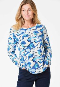 Langarmshirt in Blau, Weiß und Hellblau mit abstraktem geometrischen Muster. Weicher Stoff, runder Ausschnitt, lockere Passform und geraffte Ärmeldetails.