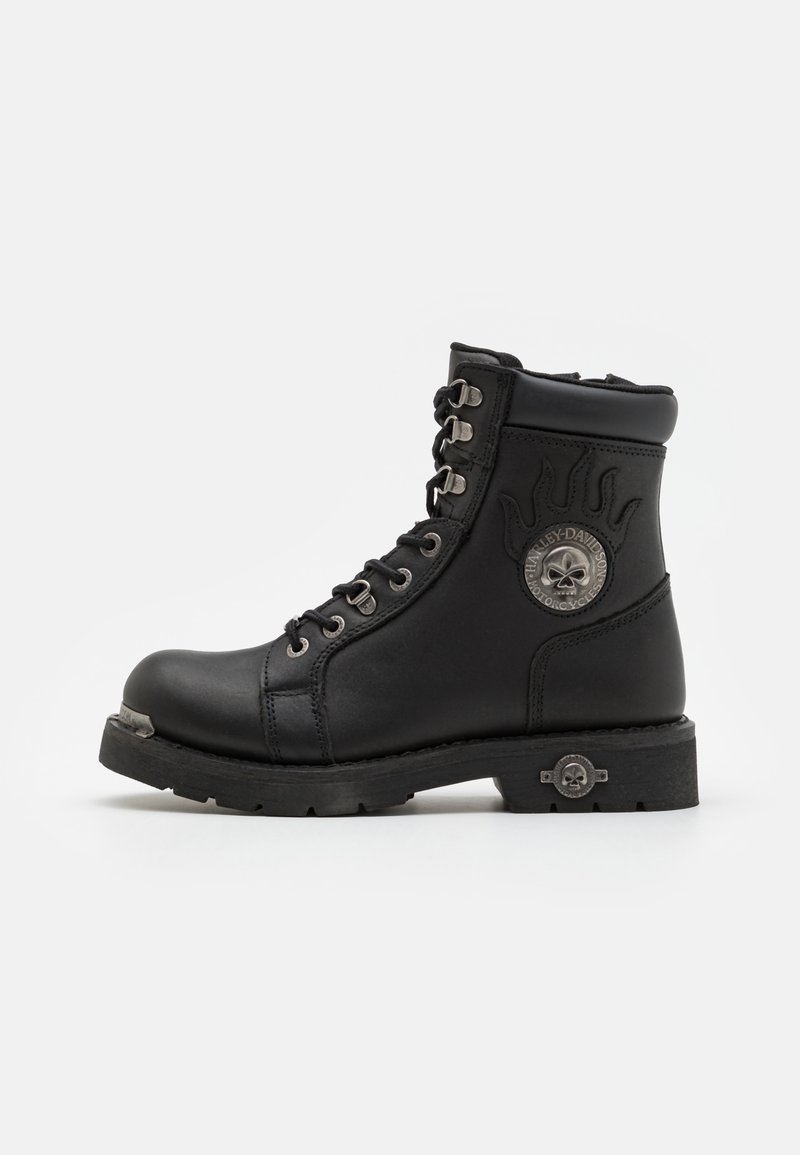 Botas de cuero negro hasta el tobillo con un cuello acolchado, ojales de metal, un logo de calavera y una suela de goma resistente. Cuenta con puntera y talón reforzados.
