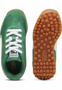Zapatillas verdes y blancas con parte superior de tela texturada, cordones blancos y una suela de goma con patrón que presenta agarres circulares.