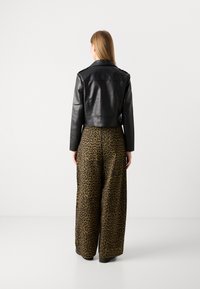 Veste en cuir noire cropped associée à un pantalon taille haute, large, revêtu d'un motif léopard noir et marron.
