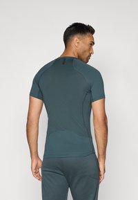 T-shirt de sport à manches courtes en bleu Sarcelle foncé, présentant un design ajusté, un tissu texturé et un accent subtil au niveau du col.