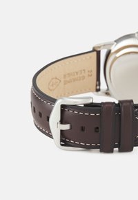 Bracelet de montre en cuir marron avec coutures blanches, boucle en argent et marquage gravé. Texture lisse avec perforations pour réglage.