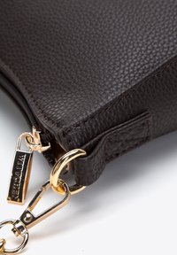 Borsa a spalla in pelle marrone con superficie testurizzata, dotata di chiusura in metallo dorato e dettagli con cerniera, e un'etichetta con il logo WITTCHEN.