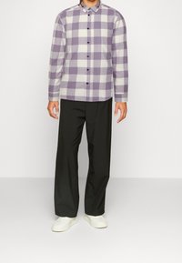 Lila-weißer Karomuster-hemd mit langen Ärmeln und Button-Down-Kragen, kombiniert mit schwarzen Hosen und weißen Sneakers.