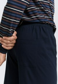 Pantalon bleu marine avec taille élastique, texture douce et poche arrière. Coordonné avec une chemise à manches longues à rayures multicolores.