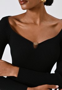 Top in maglia a coste nera con scollatura a V e dettaglio a chiave arricchito da un elemento in metallo dorato. Maniche lunghe con polsini aderenti.