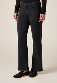 Sorte denim flare jeans med frynset kant, fem lommer og lukning med knap foran. Båret med sorte, glitrende slip-on sko.