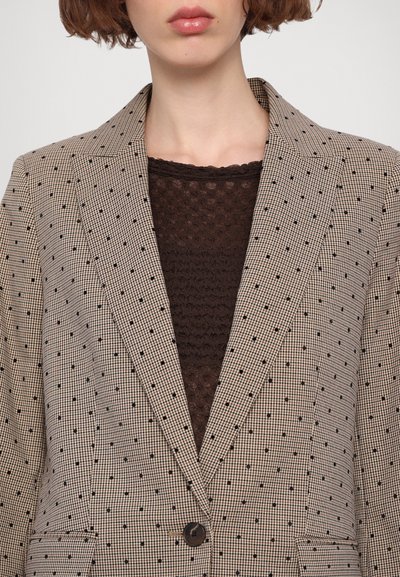 Brun og sort mønstret blazer med spids flip, enkelt knap og struktureret pasform, båret over en tekstureret brun top.