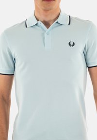 Polo shirt azzurro chiaro realizzato in un tessuto testurizzato, con una placca con bottoni, una striscia di contrasto sul colletto e un logo ricamato sul petto.
