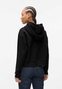 Black cropped hoodie with a drawstring hood and ribbed cuffs, paired with dark denim jeans. Features a smooth texture and relaxed fit.