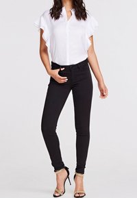 Blusa bianca a maniche corte con bottoni, abbinata a jeans skinny neri e sandali con tacco alti neri con rifiniture dorate.