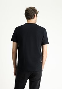 Camiseta negra de manga corta, con cuello redondo, tejido suave, diseño ajustado, lisa sin patrones ni adornos, combinada con jeans oscuros.