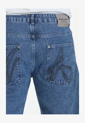 Pantalones vaqueros de denim en azul medio con un acabado texturizado. Presentan bolsillos tipo parche con costuras elevadas en hilo oscuro y una etiqueta de cuero con la marca en la cintura.