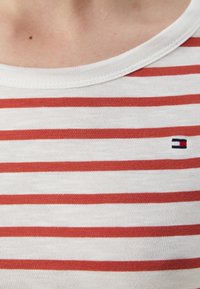T-shirt in cotone con collo a girocollo, caratterizzata da righe orizzontali rosse su sfondo bianco e un piccolo logo nell'angolo in basso.