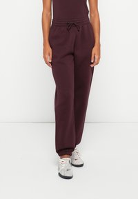 Bordeaux jogger broek gemaakt van zachte stof met een elastische tailleband, trekkoord en geribde enkels. Gecombineerd met lichte sneakers.