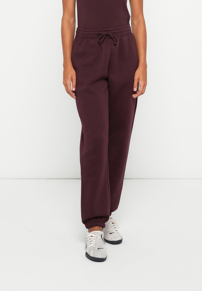 Bordeaux jogger broek gemaakt van zachte stof met een elastische tailleband, trekkoord en geribde enkels. Gecombineerd met lichte sneakers.