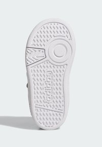 Bílá podrážka tenisky s texturovaným gumovým povrchem a rybí kostkou, s kruhovým emblémem. Vystouplé logo "adidas".