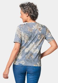 Kurzärmliges Blumenshirt in Hellblau mit cremefarbenen und braunen Mustern; weicher Stoff mit lässigem Schnitt und Rundhalsausschnitt, kombiniert mit blauen Jeans.