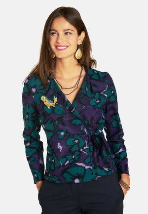 Fleece cardigan in dark purple and teal floral pattern, featuring a wrap design, ties at the waist, and a gold brooch accent.