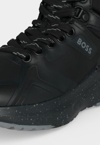 Черна висока маратонка с шарени връзки и петниста подметка, с логото "BOSS" на страничната част.