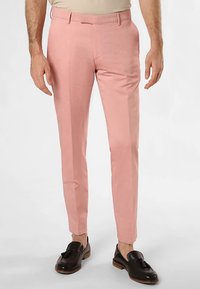 Pantaloni rosa chiaro con una vestibilità sartoriale, fronte piatto, passanti per cintura e tasche laterali. Indossati con mocassini di pelle scura. Tessuto liscio.
