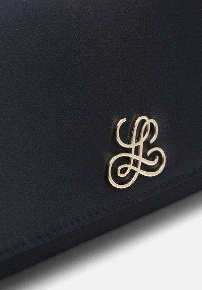 Détail du logo double L entrelacé doré sur une surface de tissu noir lisse, cousu le long du bord inférieur.