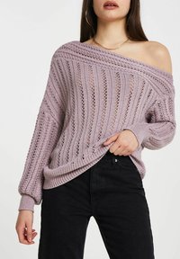 Pull tricoté violet clair avec texture côtelée et motif à mailles ouvertes. Encolure large décolletée et manches ballon. Porté sur un jean noir.