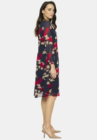 Granatowa sukienka w kwiaty z czerwonymi i beżowymi motywami, z długimi rękawami i luźnym krojem. Materiał jest lekki i lekko przezroczysty.
