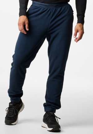 Dunkelblaue Fleece-Jogginghosen mit elastischem Bund und Bündchen, entspannter Schnitt und seitlichen Taschen. Getragen mit schwarzen Sportschuhen.