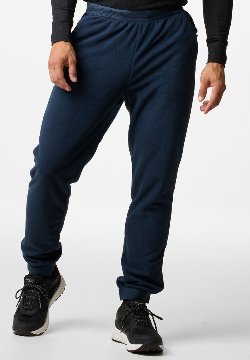 Marineblauwe fleece joggers met een elastische tailleband en manchetten, met een comfortabele pasvorm en zijzakken. Draagt bij zwarte sportschoenen.