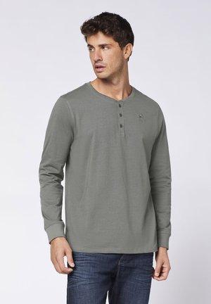 Langarm-Henley-Shirt in Olivgrün mit drei schwarzen Knöpfen an der Vorderseite, weicher Textur, rundem Ausschnitt und gesticktem Logo.